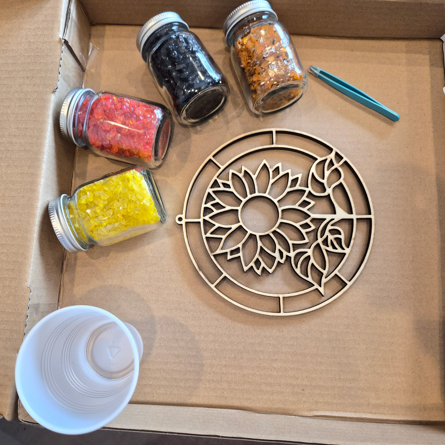 DIY crushed glass resin suncatcher kit featuring a sunflower mold, colorful crushed glass jars, and tools for the workshop at The Shoppes Off Trade in Greer, SC.